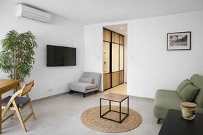 En moderne stue med et fladskærms TV, en grøn sofa, et træspisebord med stole, et lille sofabord og en stor stueplante.