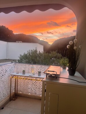 En balkon med udsigt til en solnedgang, et bord med en plante og en hvid væg.