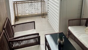 Un balcón con mobiliario de mimbre, una mesa y vistas a árboles y vegetación.