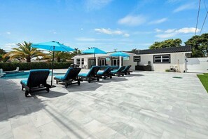 Ein Poolbereich mit Liegestühlen und Sonnenschirmen, ein Schwimmbecken und ein Gebäude mit großen Fenstern.