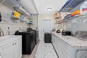 Eine kleine Küche mit Waschmaschine, kompaktem Kühlschrank und einer Arbeitsfläche mit diversen Gegenständen.