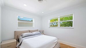 Une chambre à coucher avec un lit, deux fenêtres, une table de chevet et un radiateur.