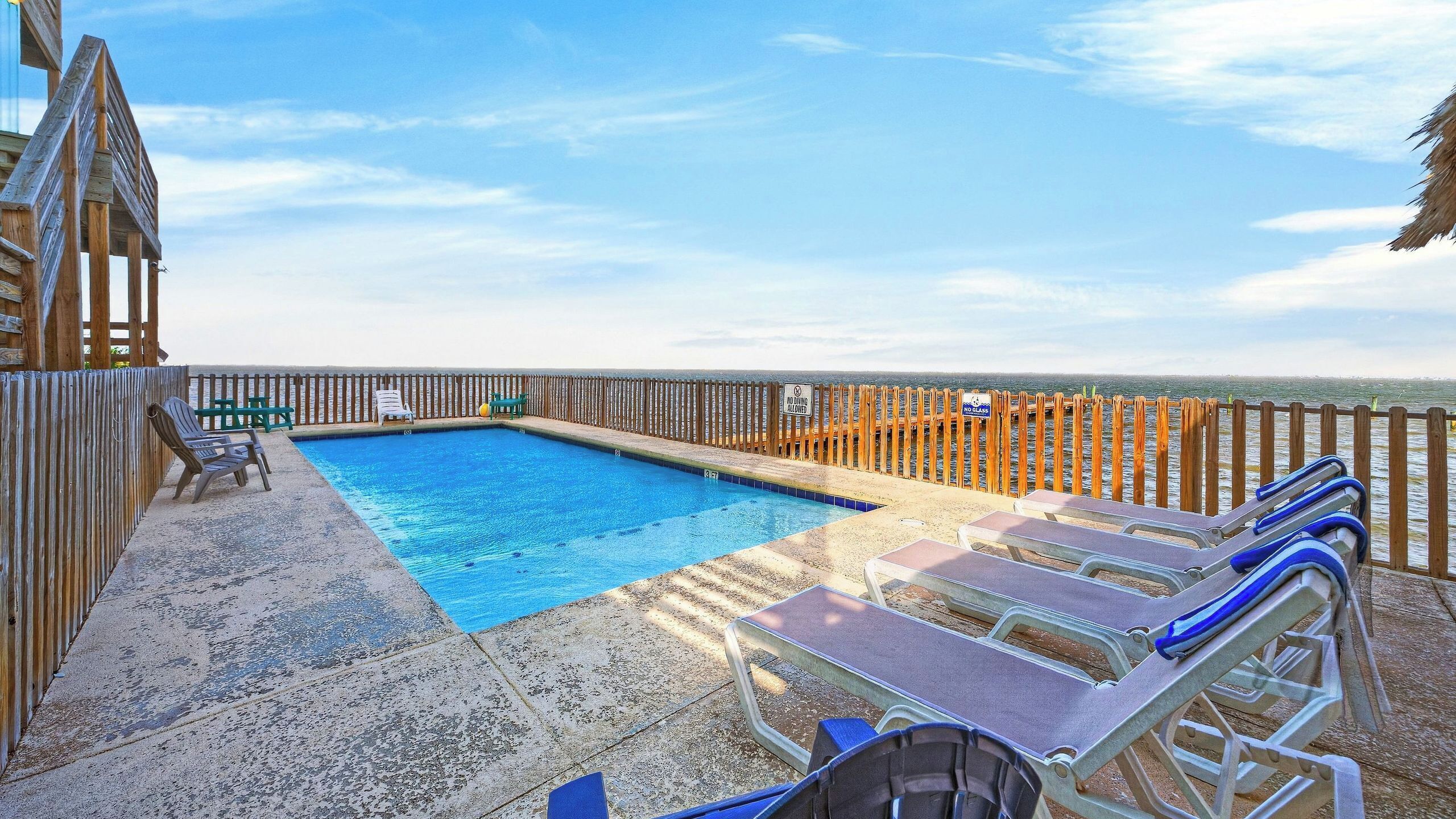 A pool area with a wooden deck, lounge chairs, and a 'No Glass Allowed' sign.