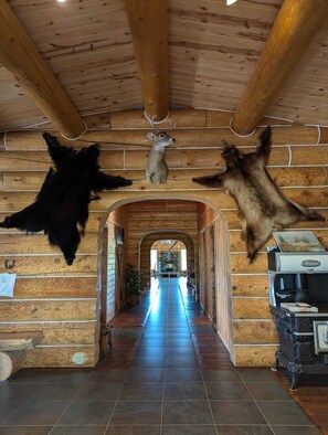 A log cabin interior with a central hallway, wooden walls, and mounted animal pelts.