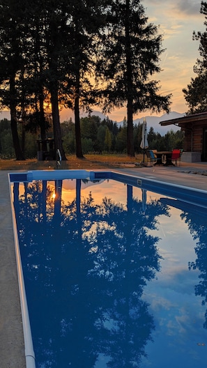 A swimming pool with a view of trees and a sunset.