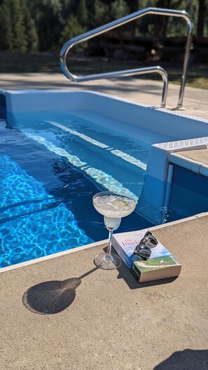 A swimming pool with clear water, a glass of a clear liquid, and a book titled 'Die Insel' on the edge.