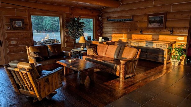 L’intérieur d’une cabane en rondins, avec une cheminée, des meubles en bois et une vue sur l’extérieur.