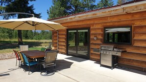 Une cabane en bois dotée d’une terrasse, d’un barbecue extérieur et d’une table avec des chaises.