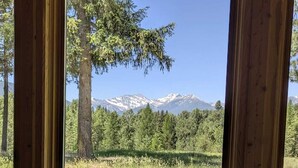 Une fenêtre à cadre en bois donnant sur une chaîne de montagnes, un arbre et un champ verdoyant.