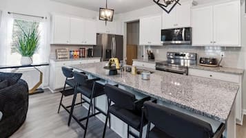A modern kitchen with granite countertops, stainless steel appliances, and bar stools.