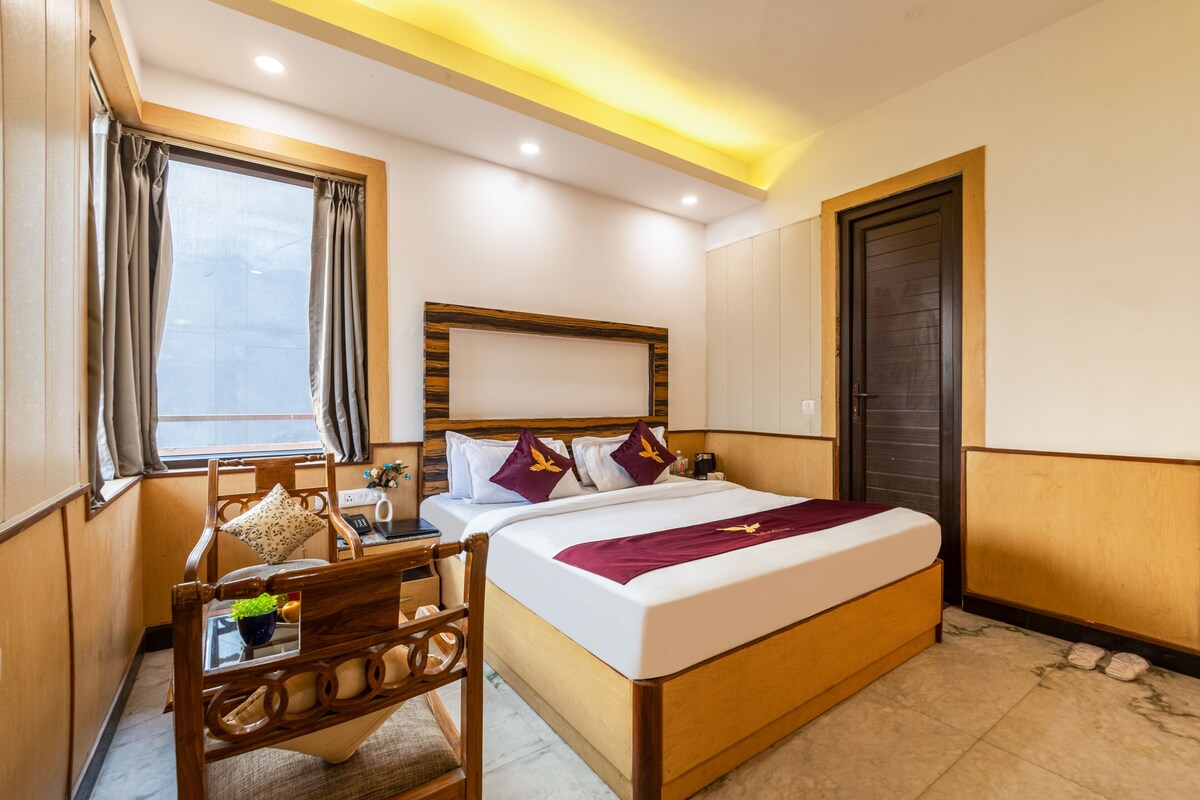 A hotel room with a bed, bedside table, chair, and a window with curtains.