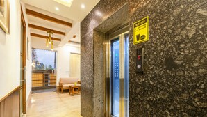 A hotel lobby with a marble wall, an elevator, a wooden bench, and a dining area with a table and chairs. - OnlyStay Aspire Inn Sector 44 Noida (Noida)
