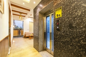 A hotel lobby with a marble wall, an elevator, a wooden bench, and a dining area with a table and chairs. - OnlyStay Aspire Inn Sector 44 Noida (Noida)