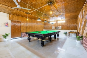 A pool table in a room with wooden walls and ceiling, a ceiling fan, and potted plants. - OnlyStay Aspire Inn Sector 44 Noida (Noida)