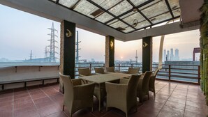 A terrace with a table and chairs, a view of the city skyline, and a sunset. - OnlyStay Aspire Inn Sector 44 Noida (Noida)