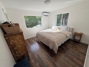 Ein Schlafzimmer mit einem Bett, zwei Fenstern, einer Holzkommode und einem kleinen Nachttisch.