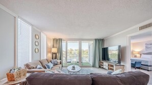 En moderne stue med sofa, sofabord og fjernsyn. Der er en balkon med udsigt.
