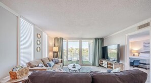Ein modernes Wohnzimmer mit Sofa, Couchtisch und Fernseher. Ein Balkon bietet einen Ausblick.