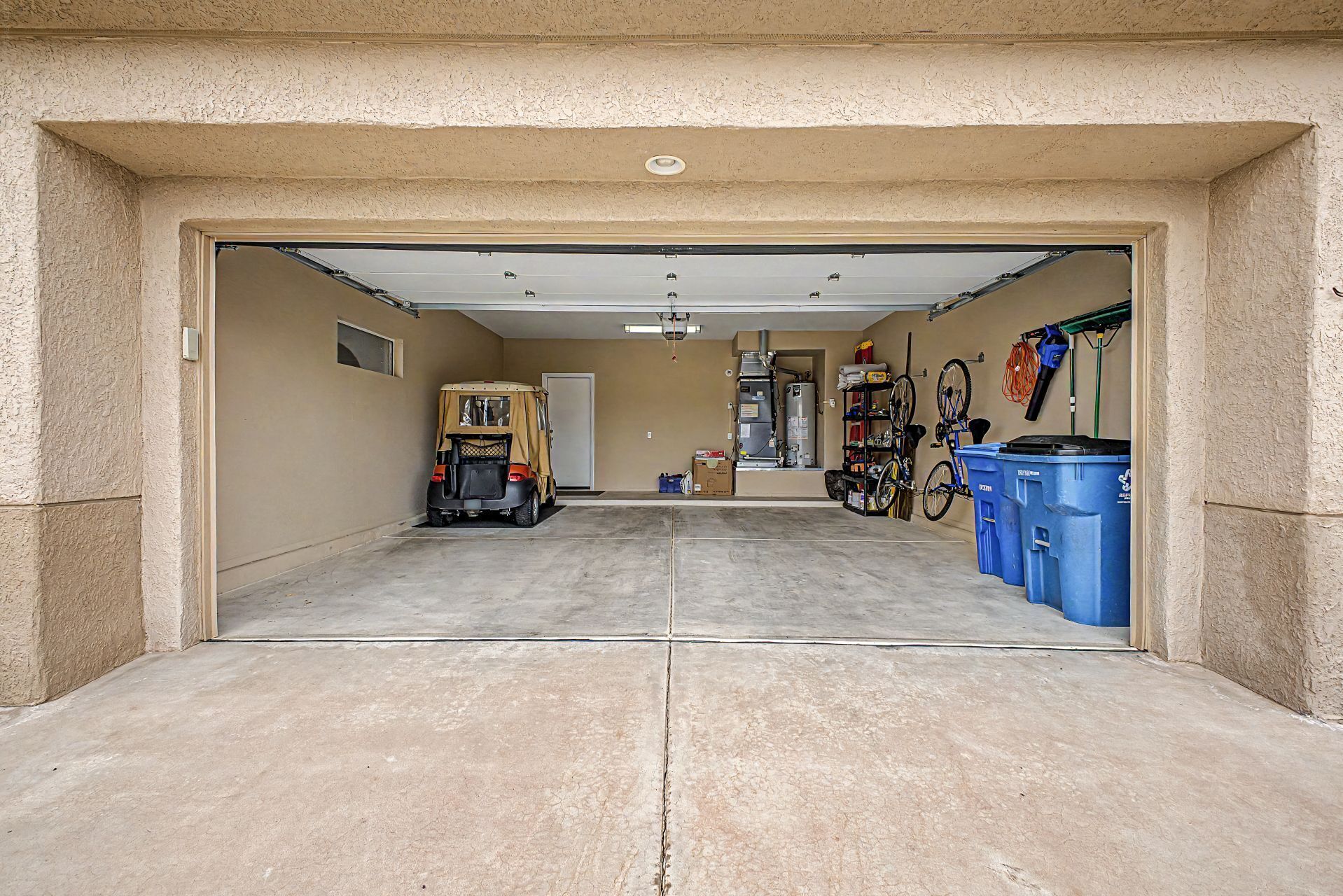 A garage with a vehicle, a bicycle, and blue trash bins.