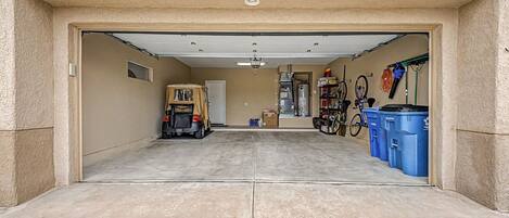 A garage with a vehicle, a bicycle, and blue trash bins.