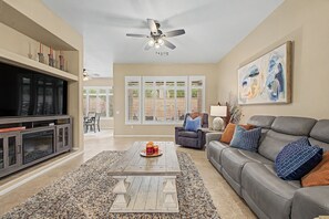 Ein Wohnzimmer mit Fernseher, Deckenventilator, Sofa, Couchtisch und einem Gemälde an der Wand.