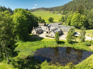 Une propriété rurale comprenant une grande maison, plusieurs bâtiments plus petits et un étang.