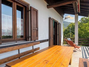 Eine Holzterrasse mit einer Bank und einem Tisch, ein Balkon mit einem Stuhl und Blick auf einen Berg.