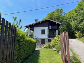 Ein modernes, zweistöckiges Haus mit Natursteinfassade, einer Holzterrasse und einem umzäunten Garten.