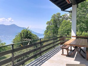 Eine Holzbänke und ein Tisch auf einer Terrasse mit Blick auf einen See und Berge.