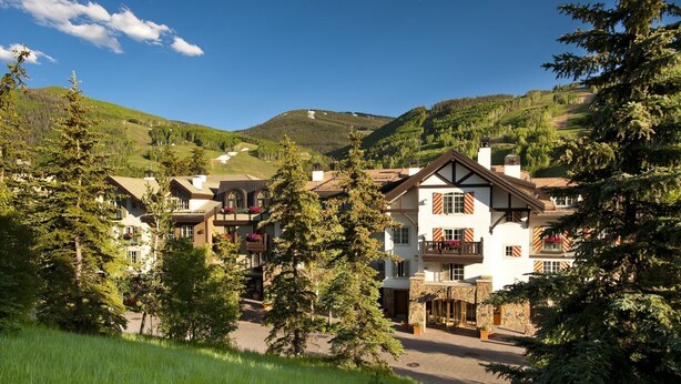 Un hotel in stile chalet tradizionale con numerosi balconi, immerso nel verde e con le montagne sullo sfondo.