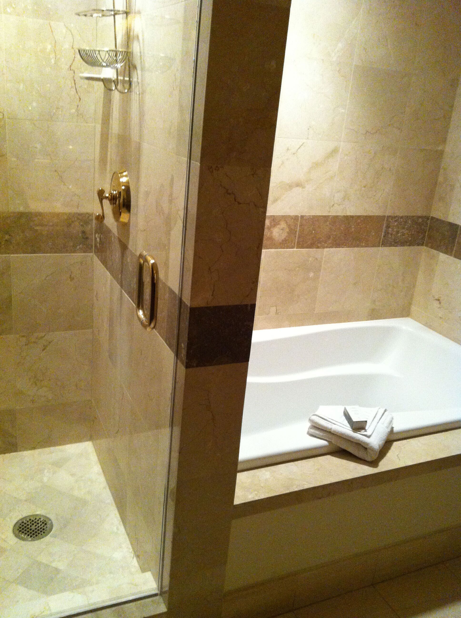 A bathroom with a shower, a bathtub, and a towel on the edge.