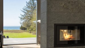 Une cheminée moderne avec une façade en verre, une terrasse en bois et une vue sur l’océan.