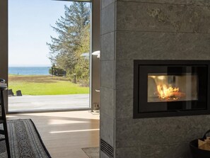 Ein moderner Kamin mit Glasklappe, eine Holzterrasse und Blick auf den Ozean.