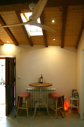 Une pièce avec un plafond en bois, une table ronde accompagnée de deux tabourets, un radiateur et une petite étagère remplie de livres.