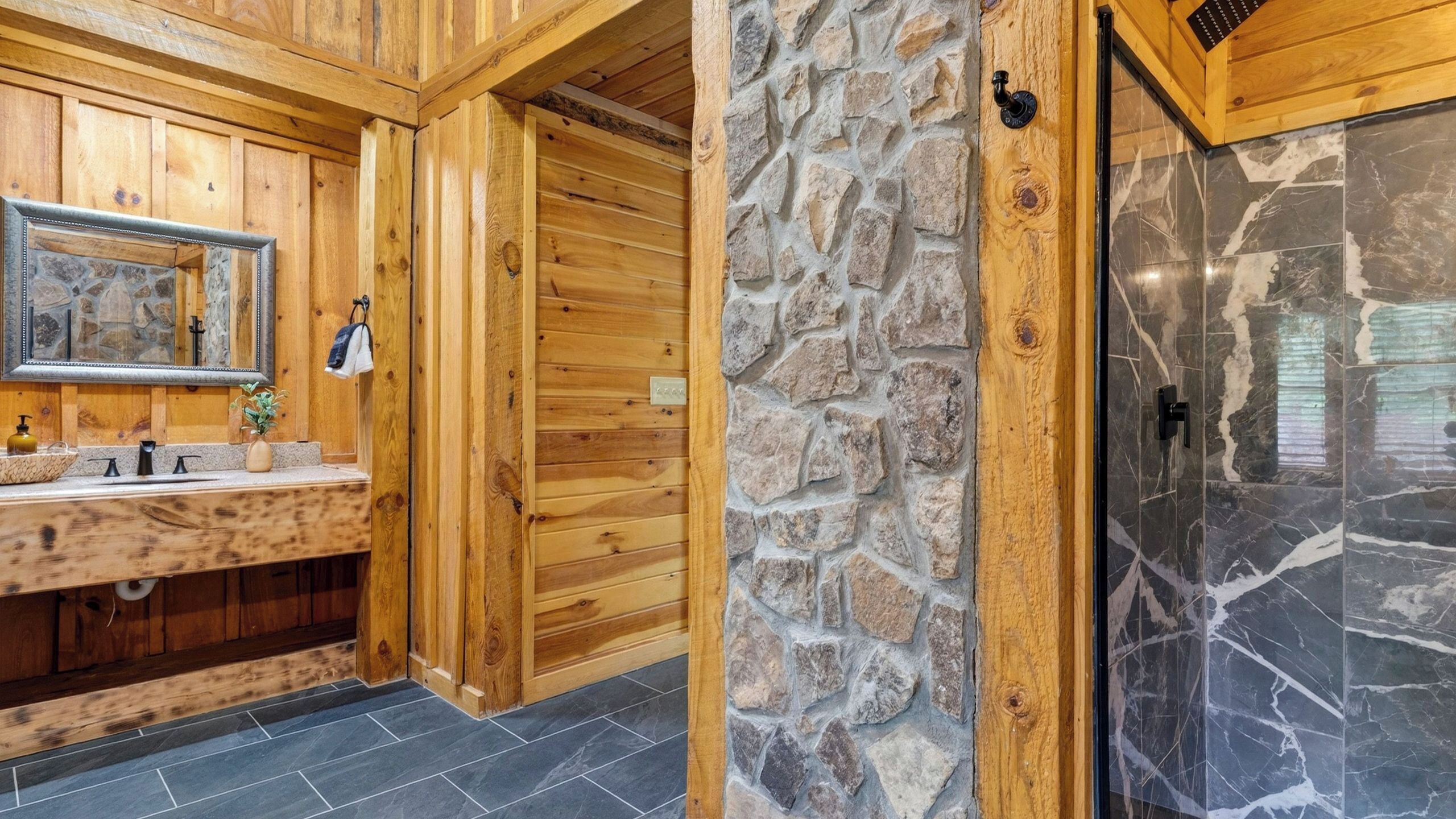 A wooden bathroom with a stone wall and a glass shower.