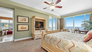 A bedroom with a large bed, a ceiling fan, a TV, and a view of the ocean. - Mediterranean West 1101 (Pensacola)