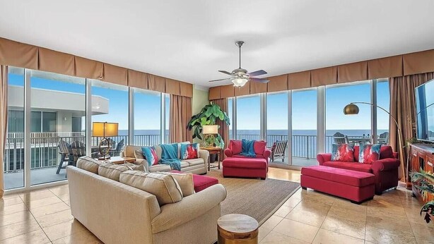 A spacious living room with large windows, a ceiling fan, and a view of the ocean. - Mediterranean West 1101 (Pensacola)