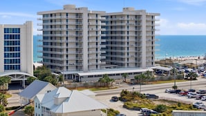 A multi-story hotel with balconies, a parking lot, and a beach view. - Mediterranean West 1101 (Pensacola)