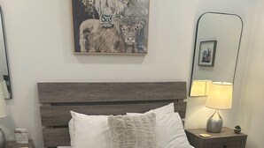 A neatly made bed with a fluffy throw, a wooden headboard, and a nightstand with a lamp and a small plant. - Walkable Gulch Condo- Sleeps 8- Gorgeous Pool (Nashville)