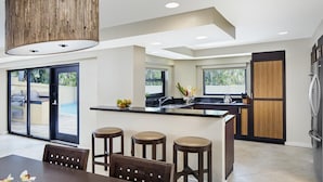 Cozinha moderna com ilha central, banquetas e vista para uma piscina.