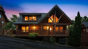 A log cabin with a porch, large windows, and a chimney. - Smokies Luxe View: Hot Tub, Fireplaces, Games+MORE (Pigeon Forge)