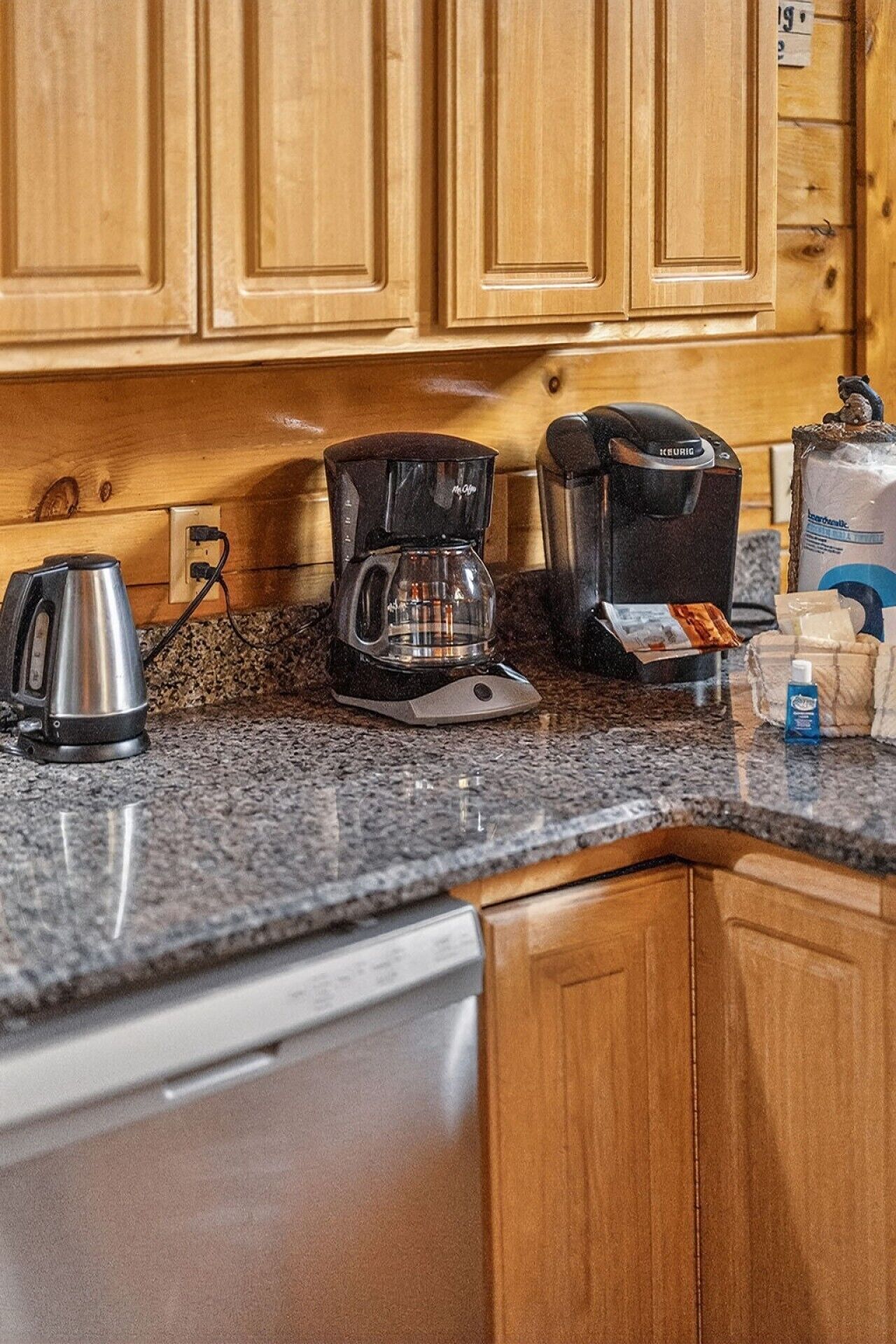 Une cuisine dotée de meubles en bois, d’une machine à café, d’une bouilloire et d’un distributeur de capsules de café.