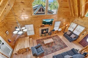 A log cabin interior with a fireplace, a sofa, a dining table, and a chandelier. - Smokies Luxe View: Hot Tub, Fireplaces, Games+MORE (Pigeon Forge)