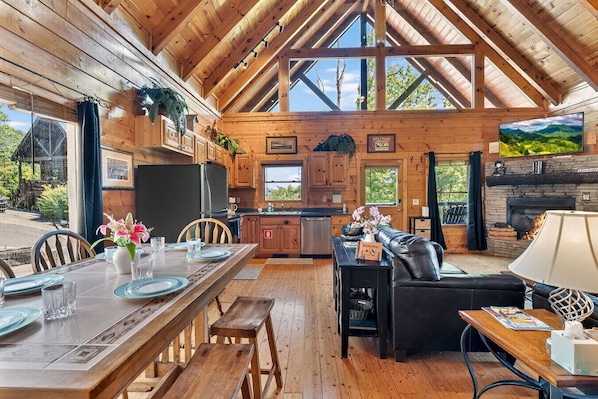 A wooden cabin interior with a dining area, kitchen, and living room. - Adohi Lodge | Panoramic Views off the Deck! (Sevierville)