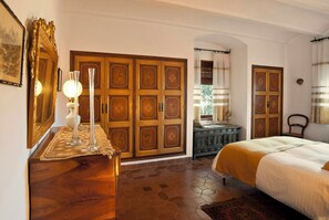 Ein Hotelzimmer mit Holzboden, einem Bett mit weißer Bettdecke, einem Nachttisch mit Lampe und einer großen Holztür mit dekorativen Feldplatten.