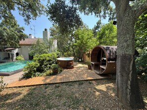 Ein Pool, eine Whirlwanne, eine Holzterrasse und eine fassförmige Struktur in einem Garten.