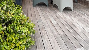 Un porxo exterior cobert amb taula i cadires de fusta, envoltat de verdura.