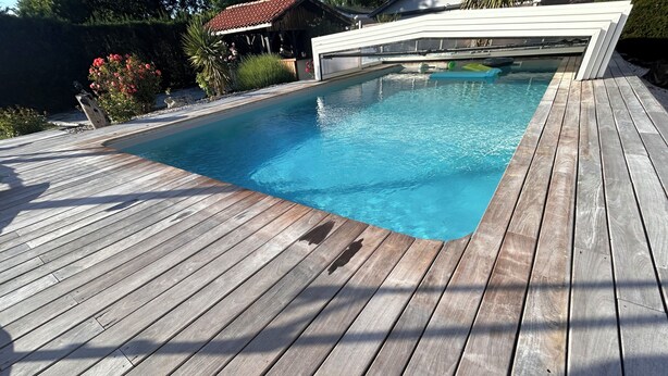 Una terrassa de fusta envoltant una piscina rectangular, amb un garatge blanc al fons.