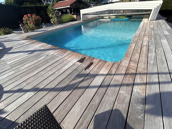 A wooden deck surrounding a rectangular swimming pool with a white garage in the background.