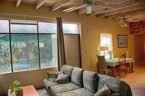 Ein Wohnzimmer mit einer Couch, einem Esstisch, Stühlen, einem Deckenventilator und großen Fenstern.